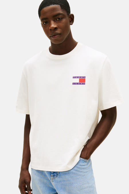 Wit T-shirt met korte mouwen van TOMMY JEANS, gedragen met een lichtblauwe jeans en een hand in de zak.
