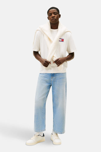 Man staand in witte Tommy Jeans T-shirt, blauwe jeans, witte trui en sneakers.