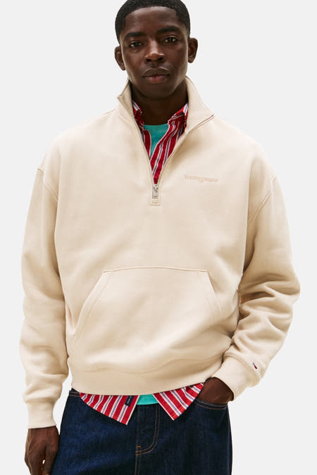 Beige sweater van TOMMY JEANS, met halve rits, buidelzak en rode gestreepte blouse eronder.
