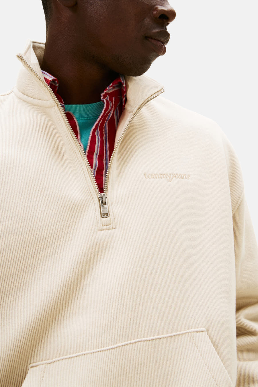 Beige sweater van TOMMY JEANS met halve rits en rode gestreepte kraag over een turquoise T-shirt.
