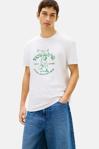 Grijs T-shirt met korte mouwen van Tommy Jeans, met groene gymprint en gedragen met een blauwe jeans.
