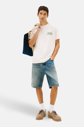 Ecru T-shirt met korte mouwen van TOMMY JEANS, met een logo print, gedragen met denim shorts en bruine schoenen.
