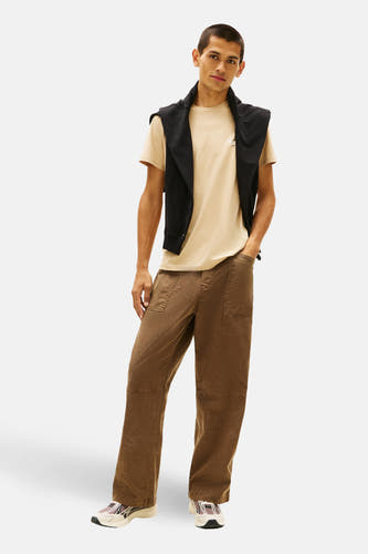 Beige T-shirt met korte mouwen van TOMMY JEANS, met een zwart vest losjes om de schouders geknoopt.