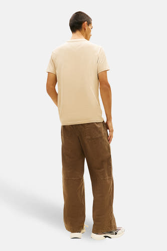 T-shirt beige à manches courtes de TOMMY JEANS, vu de dos, combiné avec un pantalon marron et des baskets.