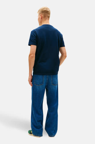 Blauw T-shirt met korte mouwen van TOMMY JEANS, gezien van achteren, gecombineerd met wijde jeans en groene schoenen.
