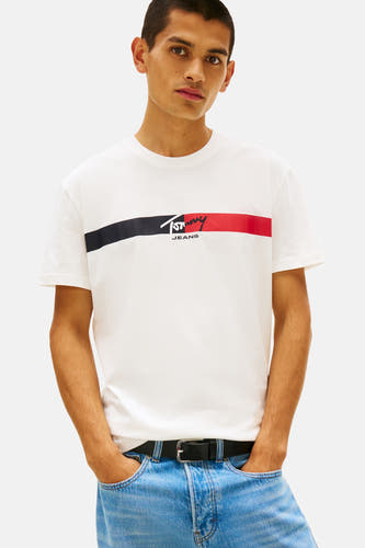Wit T-shirt met korte mouwen van TOMMY JEANS, met horizontale strepen in zwart en rood, en blauwe jeans.
