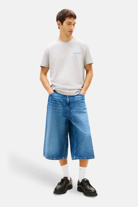 Grijs T-shirt met korte mouwen van TOMMY JEANS, met klein logo op de borst en gedragen met wijde jeans shorts.
