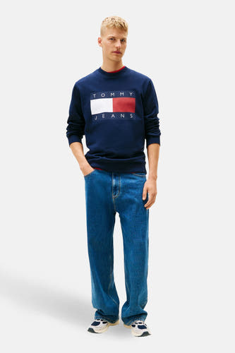 Blauwe sweater van TOMMY JEANS, met rechthoekig logo op de borst, gecombineerd met jeans en sneakers.
