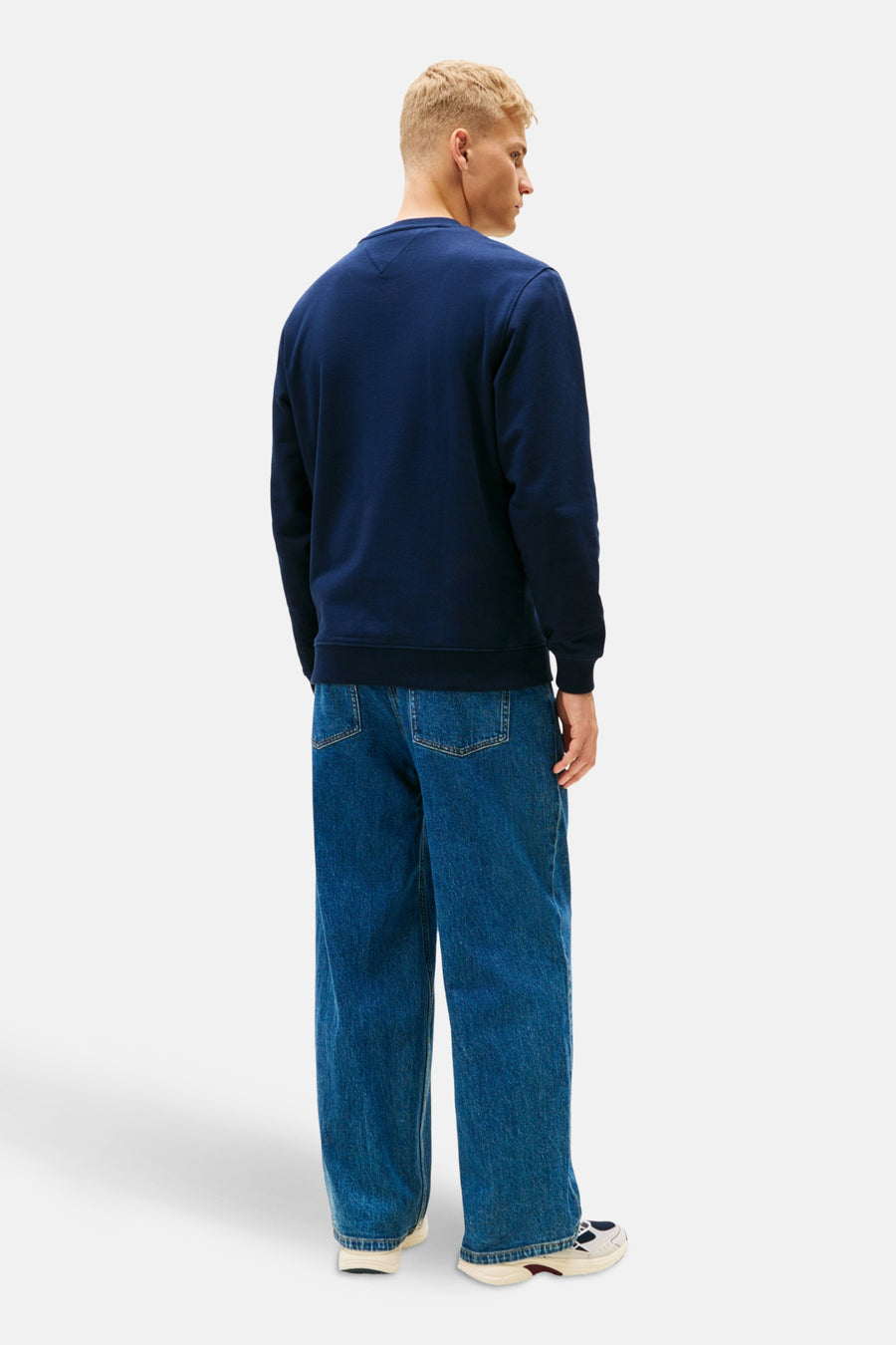 Achterkant van een man in een donkerblauw sweatshirt en wijde jeans.