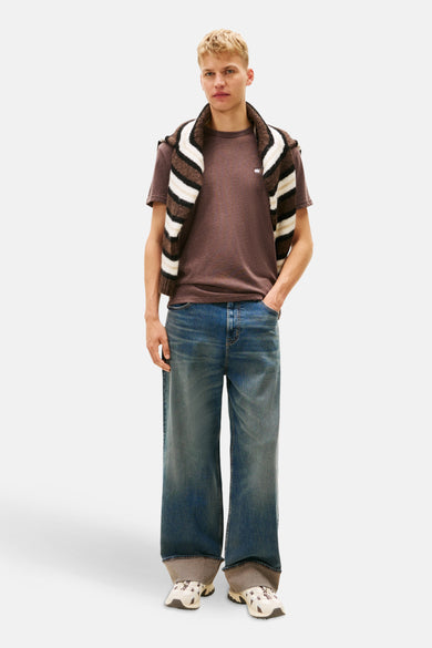 Bruin T-shirt met korte mouwen van TOMMY JEANS, met een gestreepte trui over de schouders en wijde jeans.
