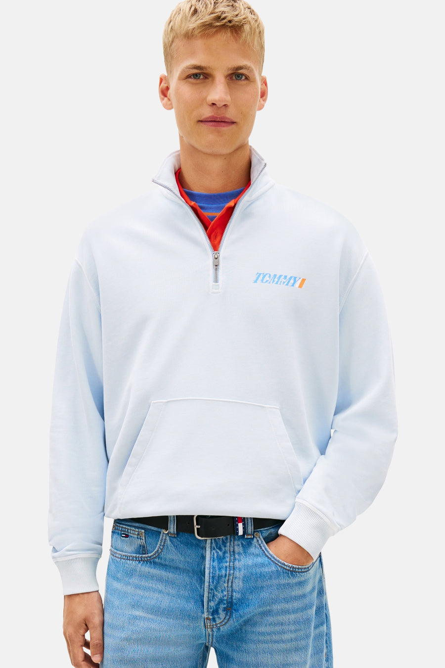 Pull bleu à col roulé de Tommy Jeans, avec une fermeture éclair courte et une coupe ample par-dessus un haut rouge.