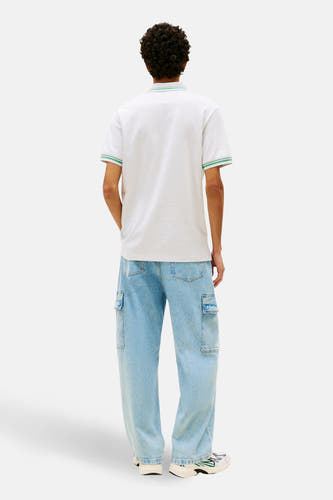 Polo grise à manches courtes de Tommy Jeans, avec une rayure verte sur le col et les manches, combinée avec un jean ample et des baskets.