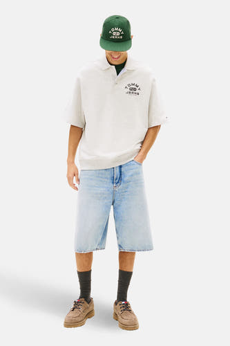 Grijs poloshirt met korte mouwen van TOMMY JEANS, met een logoprint op de borst, gecombineerd met denim shorts en bruine schoenen.