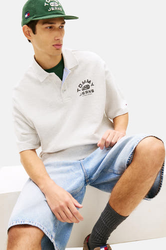 Grijs poloshirt met korte mouwen van TOMMY JEANS, met logo op de borst, gedragen met een groene top en denim shorts.
