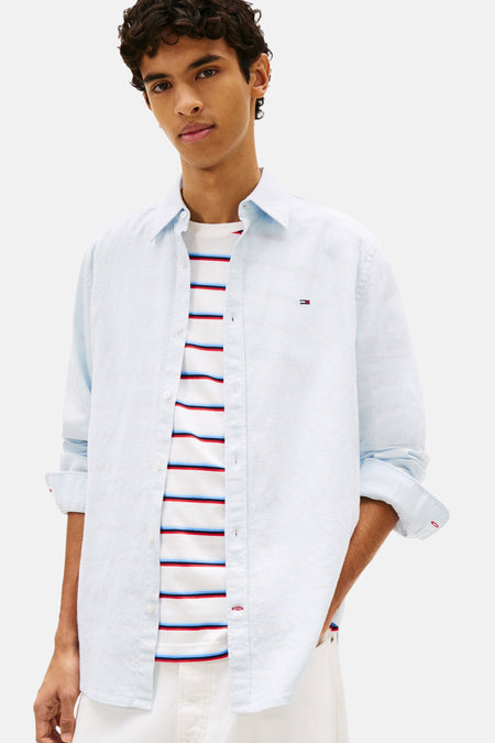 Chemise bleue de TOMMY JEANS, portée sur un haut rayé, avec un pantalon blanc et une casquette bleue.