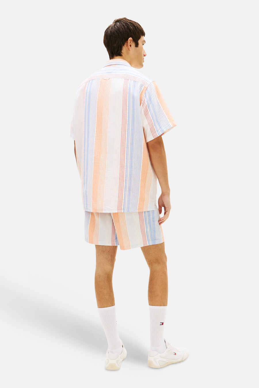 Chemise multicolore à manches courtes de TOMMY JEANS, rayée de lignes orange, bleues et rouges, avec un short assorti et des chaussettes blanches.