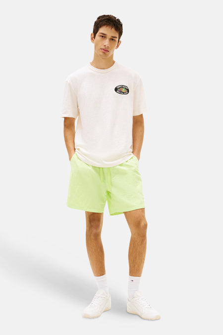 Gele short van TOMMY JEANS, gedragen door een man met een crèmekleurig T-shirt en witte sneakers.
