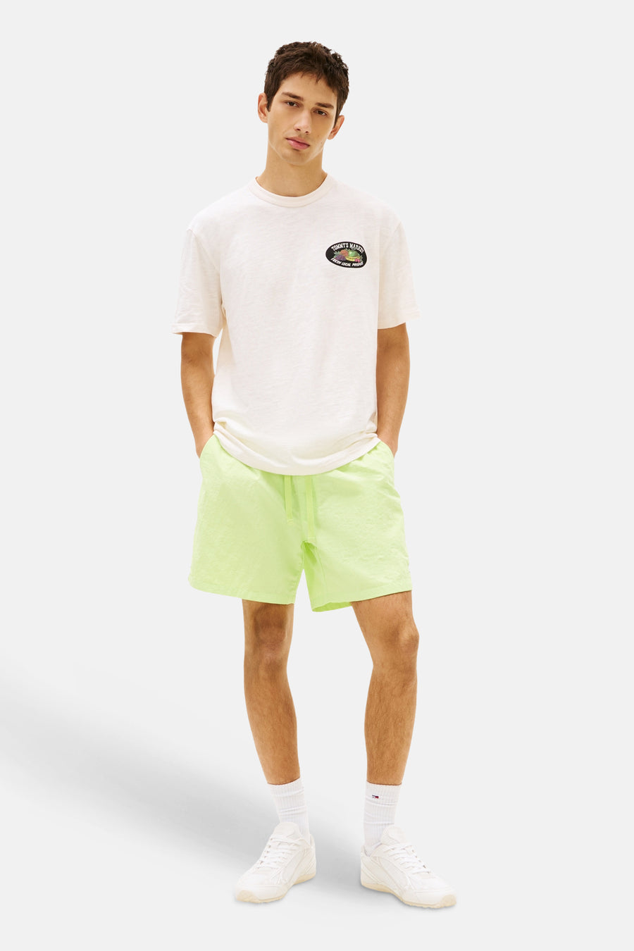 Gele short van TOMMY JEANS, gedragen door een man met een crèmekleurig T-shirt en witte sneakers.