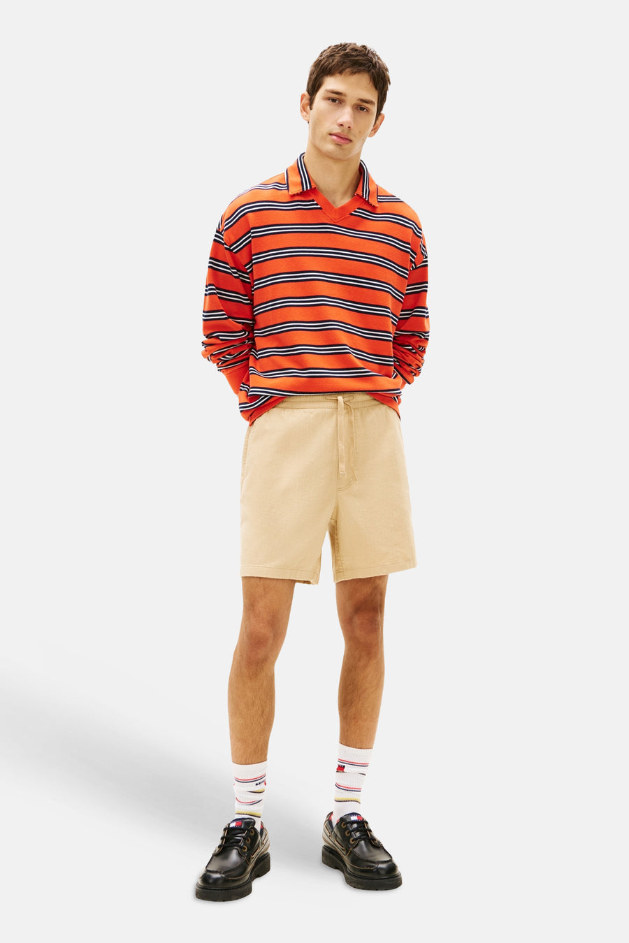 Bruine short met trekkoord van TOMMY JEANS, gedragen met een oranje gestreept polo shirt, witte sokken en zwarte schoenen.