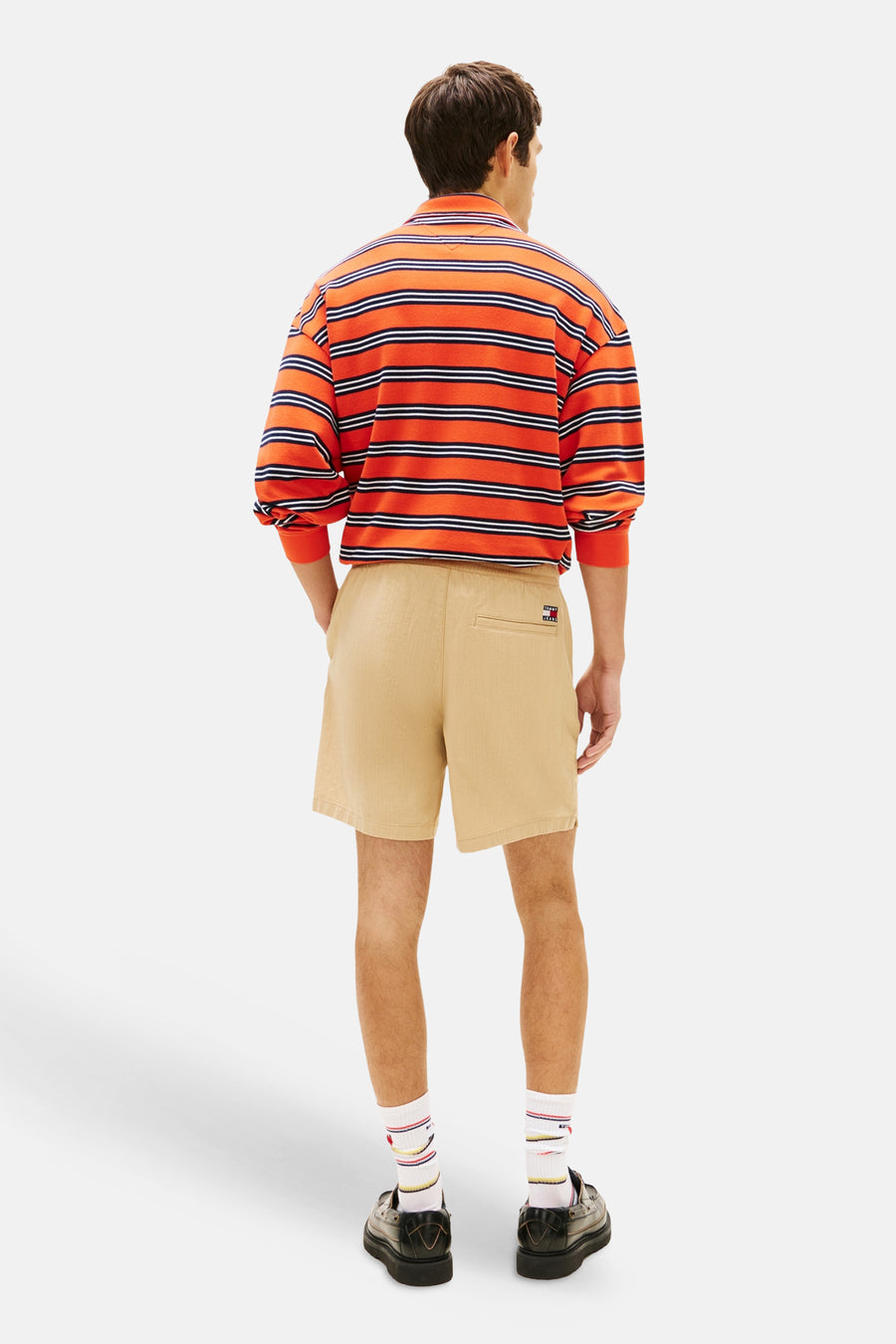 Bruine short van TOMMY JEANS met ribtextuur en logo, gedragen door model met gestreept shirt en loafers, achterzijde.