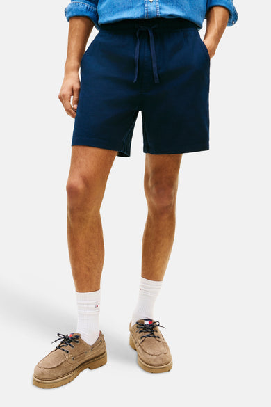 Blauwe short van TOMMY JEANS, gecombineerd met witte sokken en bruine schoenen.
