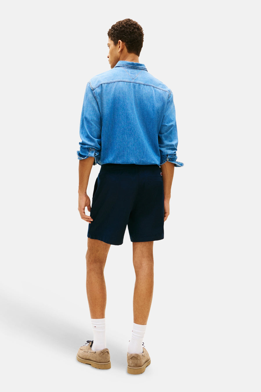 Blauwe short van TOMMY JEANS, gezien van achteren, met een denim overhemd en bruine schoenen.
