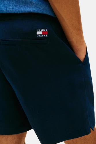 Blauwe short van TOMMY JEANS, met achterzak en hand in de steekzak.
