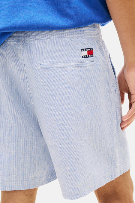 Short bleu TOMMY JEANS à fines rayures verticales, taille élastique, poche passepoilée et écusson logo à l'arrière.