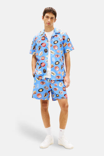 Blauwe short met print van Tommy Jeans, gedragen met een wit T-shirt en witte sneakers.
