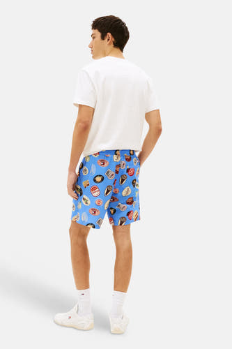 Blauwe short van TOMMY JEANS met een opvallende badgeprint, gecombineerd met een wit T-shirt en witte sokken met sneakers.
