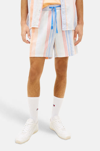 Multicolor short van TOMMY JEANS met verticale oranje, rode en blauwe strepen, blauw trekkoord, witte sokken en sneakers.