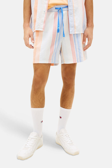 Short rayé multicolore de TOMMY JEANS, avec des rayures verticales en blanc, orange, bleu clair et rouge, porté en ensemble.