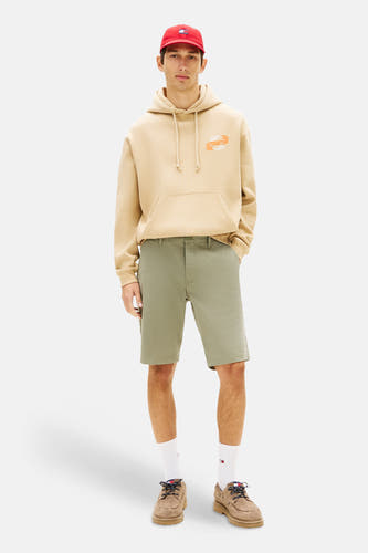 Groene short van TOMMY JEANS, gecombineerd met een beige hoodie, witte sokken en bruine schoenen.