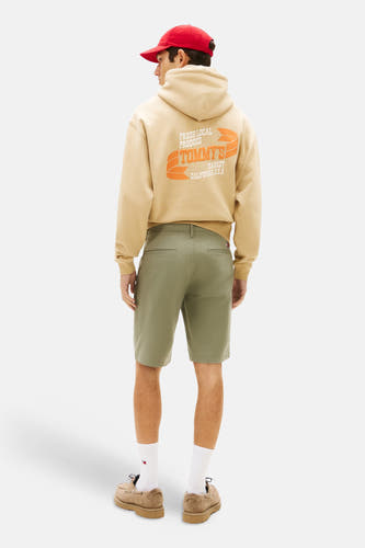 Short vert de TOMMY JEANS, vu de dos, avec un sweat à capuche beige et une casquette rouge.