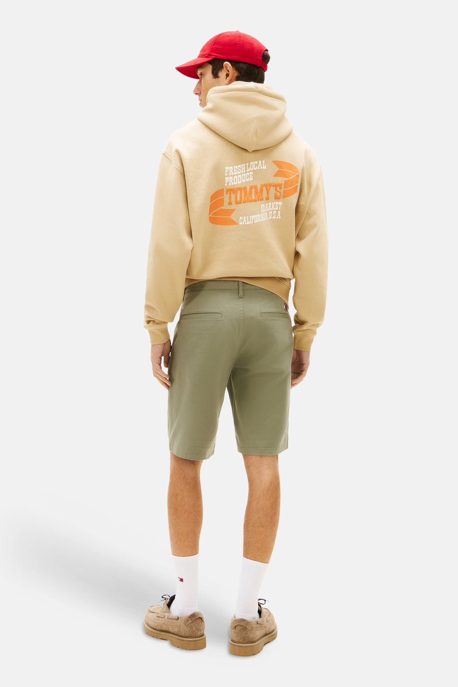 Short vert de TOMMY JEANS, vu de dos, avec un sweat à capuche beige et une casquette rouge.