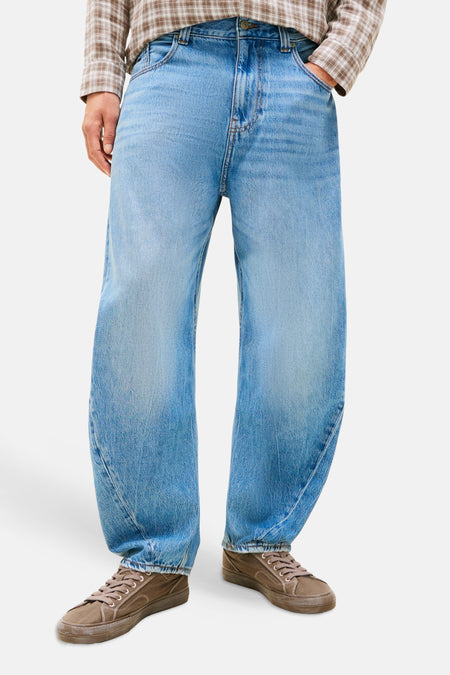 Lichtblauwe denim jeans van TOMMY JEANS met ruime pasvorm, gedragen met een geruit overhemd en bruine sneakers.