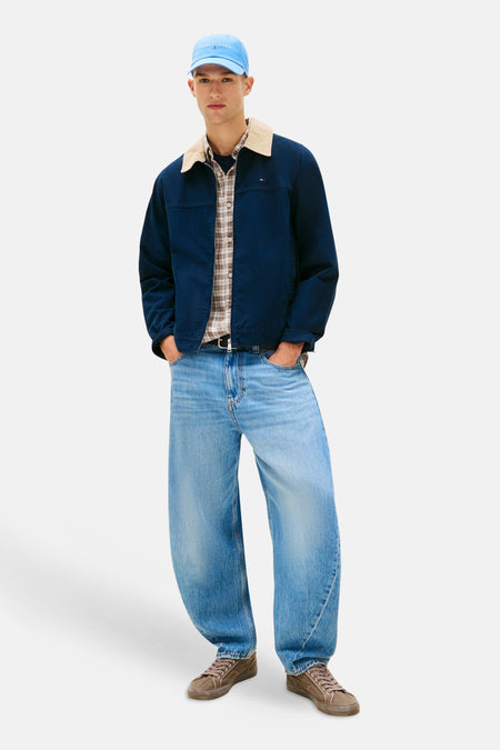 Lichtblauwe spijkerbroek met speciale pasvorm van TOMMY JEANS, gecombineerd met een donkerblauw jack, geruit overhemd en bruine sneakers.
