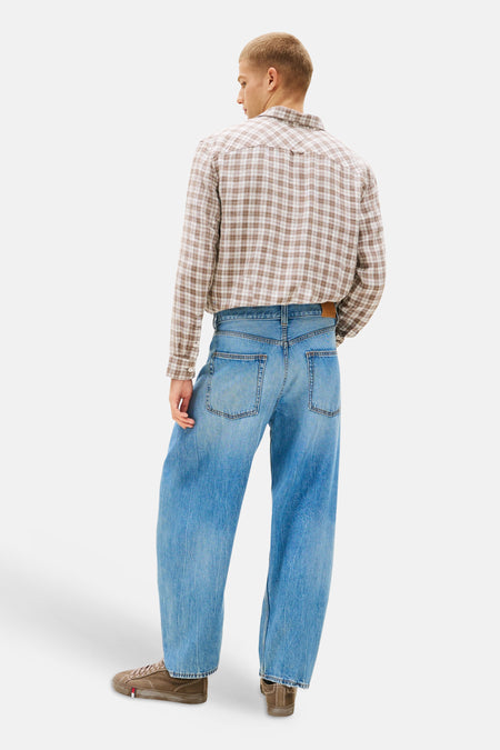 Lichtblauwe denim jeans met wijde pasvorm van TOMMY JEANS, van achteren gezien op een model met een geruit overhemd en bruine sneakers.