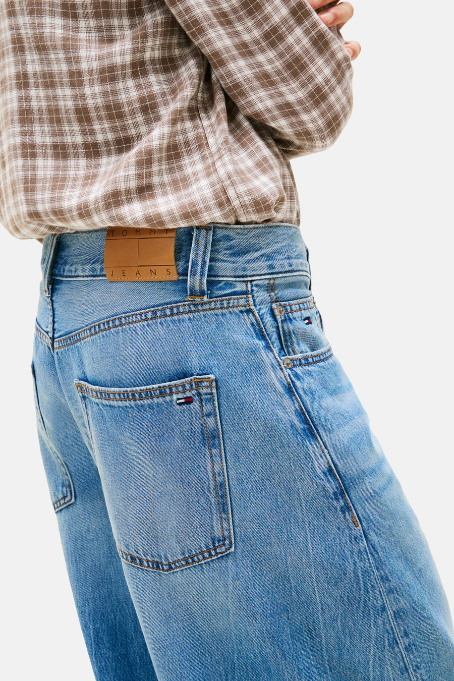 Lichtblauwe spijkerbroek van TOMMY JEANS met bruin leren logo patch op de tailleband, gecombineerd met een geruit overhemd.