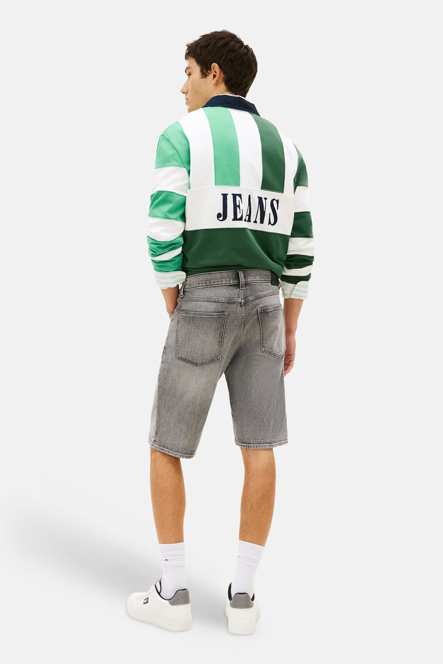 Short en jean gris en denim de TOMMY JEANS, vu de dos, avec un polo de rugby rayé et des baskets blanches.