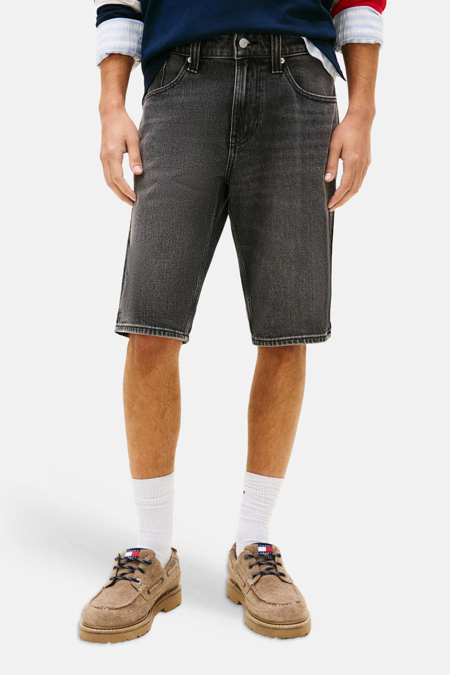 Short en jean noir de TOMMY JEANS, avec coutures et porté avec une casquette rouge, un pull rayé et des chaussures marron.