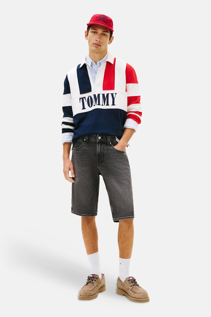 Zwarte denim short van TOMMY JEANS, met stiksels en gedragen met een rood petje, een gestreepte trui en bruine schoenen.
