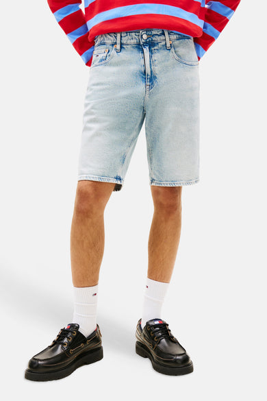 Short en jean bleu clair de TOMMY JEANS, porté avec un polo rugby rayé et des chaussures richelieu noires.