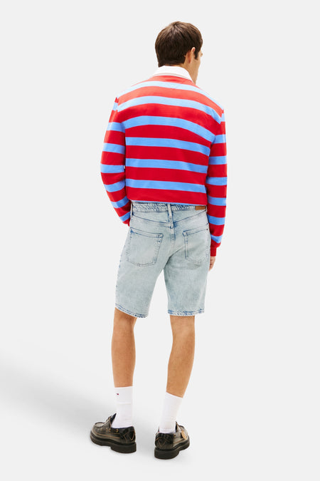 Lichtblauwe denim jeansshort van TOMMY JEANS, van achteren gezien met zichtbare achterzakken, gedragen door een man met een rood-blauw gestreept shirt en donkere schoenen.