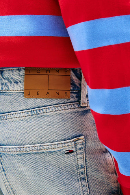 Lichtblauwe denim jeansshort van TOMMY JEANS met bruine leren patch en klein vlaglogo, gedragen met rood-blauw gestreepte trui.