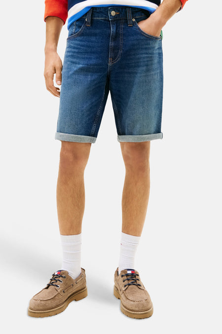 Donkerblauwe denim jeansshort van TOMMY JEANS met opgerolde pijpen, gedragen met witte sokken en bruine bootschoenen.