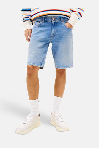 Jeansshort van middenblauw denim van TOMMY JEANS, gedragen door een man met een gestreepte trui en sneakers.
