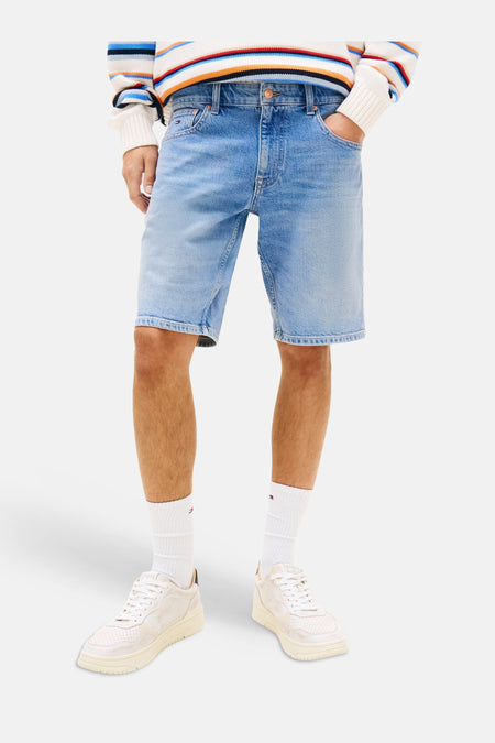 Jeansshort van middenblauw denim van TOMMY JEANS, gedragen door een man met een gestreepte trui en sneakers.