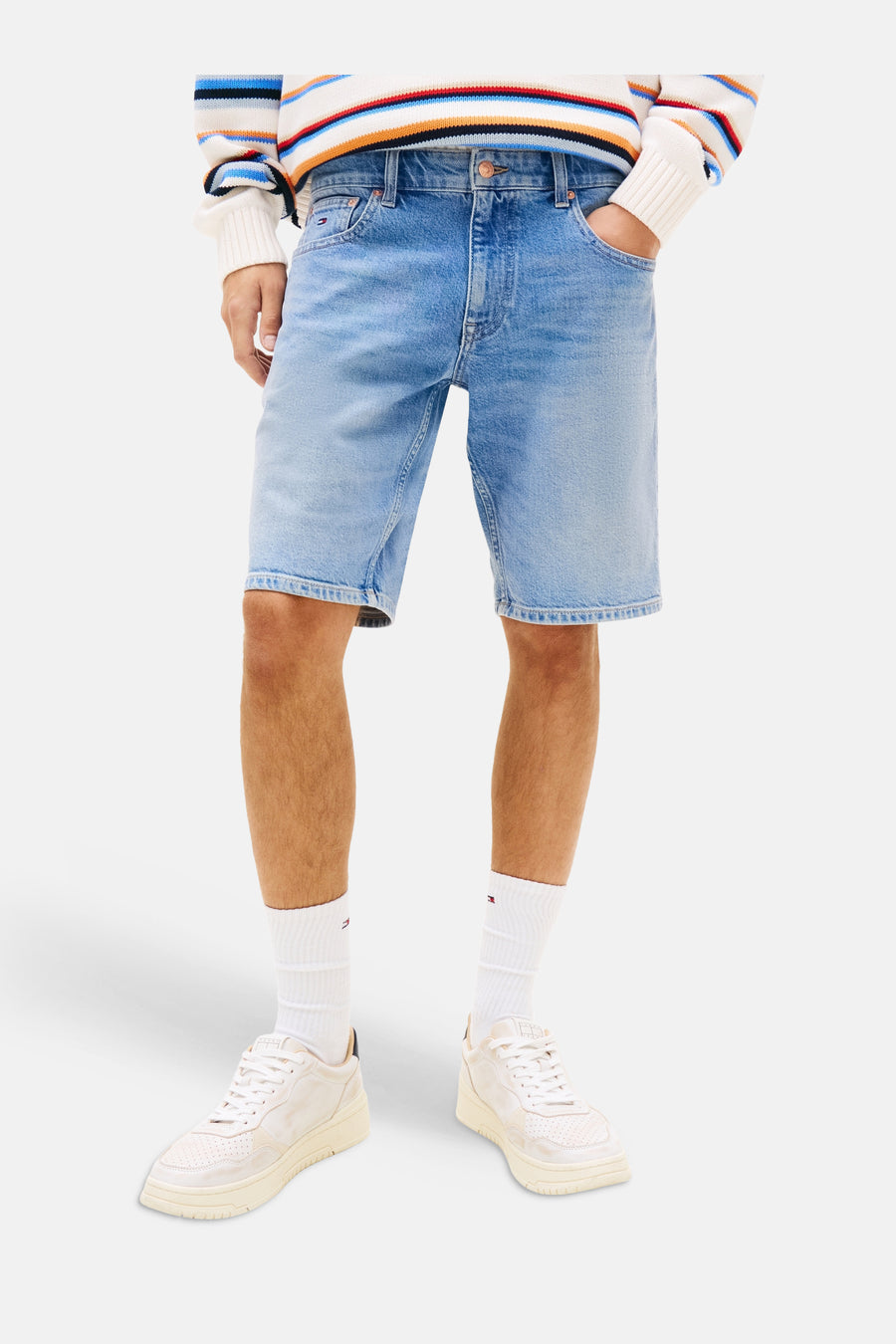 Jeansshort van middenblauw denim van TOMMY JEANS, gedragen door een man met een gestreepte trui en sneakers.