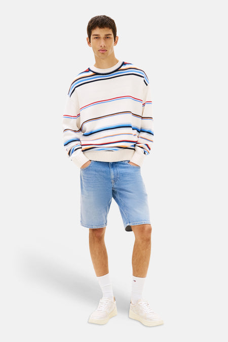 Jeansshort van mid-blauwe denim van TOMMY JEANS, gedragen door een man met een gestreepte trui en witte sneakers.